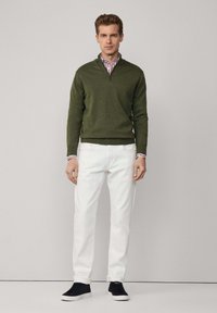 Maglione verde con zip, pantaloni bianchi e sneakers neri. Il maglione ha un collo tondo e polsini a coste. Texture liscia con una vestibilità casual.