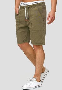 Olive green shorts made of cotton with an elastic waistband and drawstring. Features front pockets and a relaxed fit.