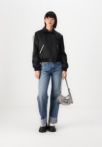 Svart bomberjakke med hvite glidelåsdetaljer, avslappede jeans, sølvveske og klumpete svarte sko. Glatt stoff og oppbrettede hems.