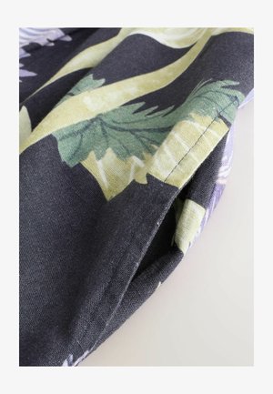 Textília s kvetinovým vzorom na tmavom pozadí; listy v zelených a žltých odtieňoch; textúrovaný povrch so viditeľnými stehmi a záhybmi.