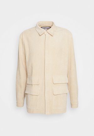 Beige kordbársony zakó, gallérral, rejtett elülső gombokkal, hosszú ujjakkal és négy hajtókás zsebbel elöl.