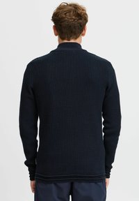 Marineblauer Strickpullover mit einem strukturierten Muster, langen Ärmeln und hohem Kragen. Rippdetails an Saum und Bündchen ergänzen das Design.