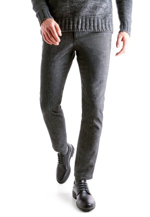 Pantaloni grigi strutturati e scarpe in pelle nere, abbinati a un maglione scuro a costine, con vestibilità slim e dettagli a motivo sottili.