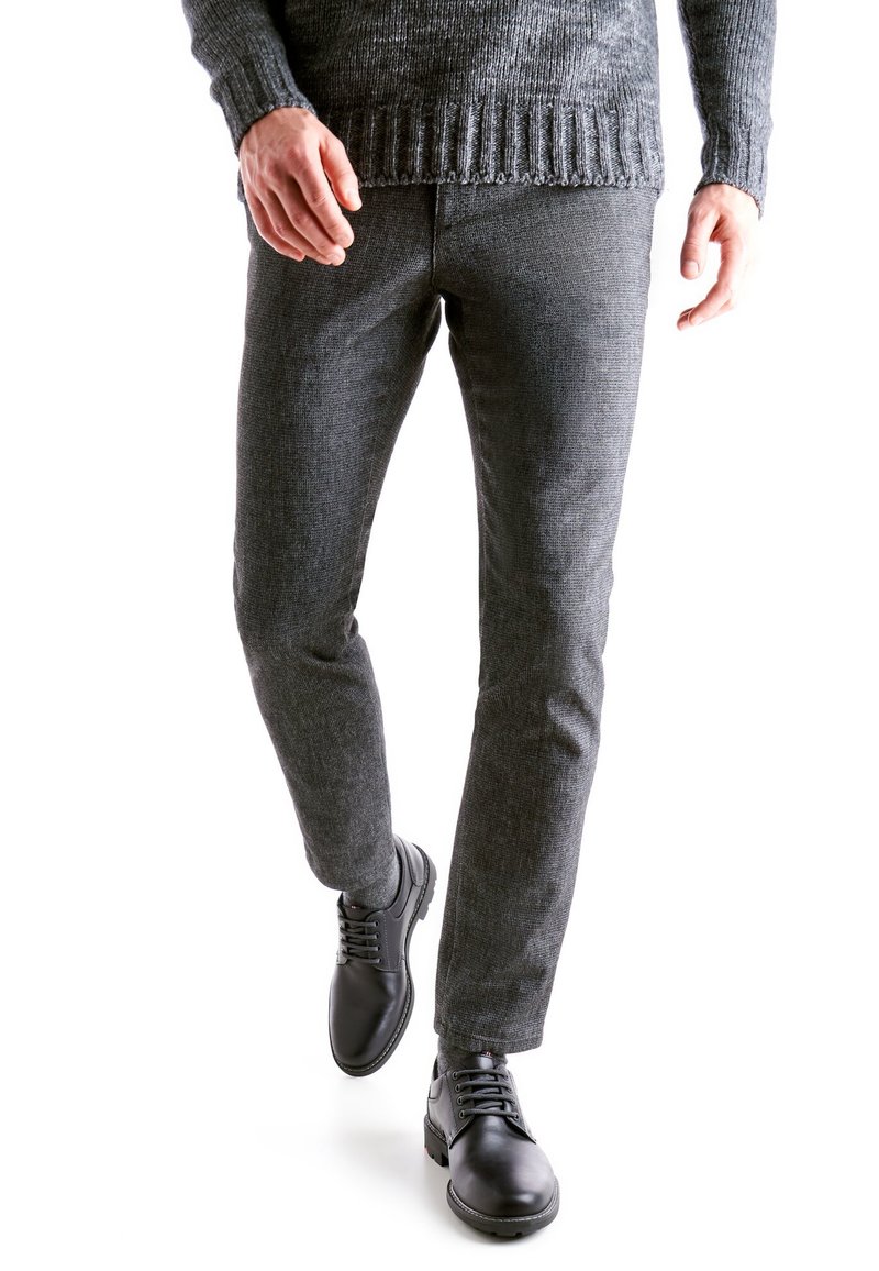 Pantaloni grigi strutturati e scarpe in pelle nere, abbinati a un maglione scuro a costine, con vestibilità slim e dettagli a motivo sottili.