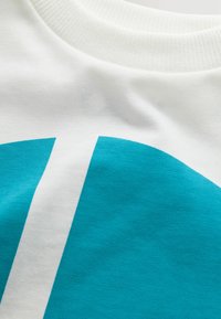 Weißes Baumwoll-T-Shirt mit grafischem Teal-Muster und weißem Streifen, geripptem Ausschnitt und glatter Textur.