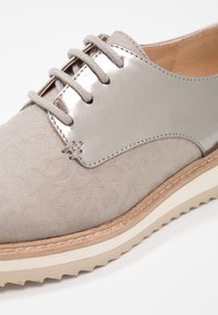 Botte grise clair avec une tige texturée et un accent métallique brillant. Conçue avec une semelle épaisse et un système de laçage.