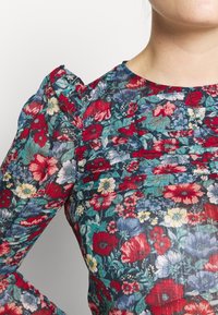 Blusa floreale con maniche a sbuffo, caratterizzata da un motivo multicolore di fiori rossi, blu e gialli su uno sfondo scuro. Accento con design plissettato.