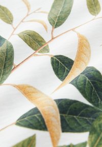 Cotton fabric featuring a botanical print with green and yellow leaves on a white background; detailed texture and layered leaves visible.