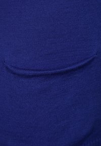 Blå stickad tyg med en slät yta, med en liten fickdetalj. Materialet är något elastiskt och tätt vävt.