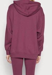 Burgundy huvtröja med avslappnad passform, ribbade muddar och nederkant samt en slät yta. Synliga sömmar längs axlarna.