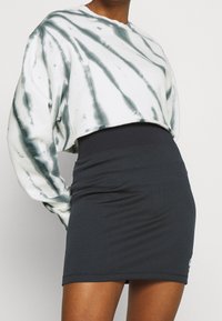 Krátká mikina bílá s zeleným batikovaným vzorem, zkombinovaná s černou mini sukní s žebrovaným vzorem a přiléhavým pasem.