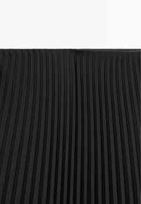 Tessuto nero a pieghe con strisce verticali, superficie texturizzata con pieghe di larghezza variabile, materiale denso con una finitura liscia.