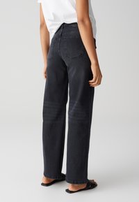 Zwarte straight-leg jeans met achterzakken, een lichte vervaging en een klassieke denimtextuur. Draagt met zwarte platte sandalen.