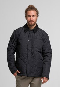 Czarna kurtka pikowana z kołnierzem z szerokiego materiału, zapinana na napy z przodu, z jedną kieszenią na piersi. Posiada wzór w diamenty i długie rękawy.