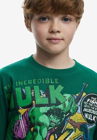 Grön sweatshirt med grafik av "The Incredible Hulk", fet text och serietidningsillustrationer. Tillverkad i bomull med rundad hals.