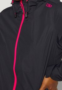 Veste noire avec une fermeture éclair rose et des accents, dotée d'une capuche et de cordons de serrage ajustables, fabriquée en matériau léger et texturé.