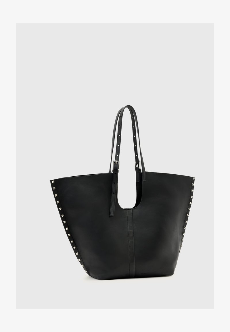 Černá kožená taška přes rameno s širokým otvorem, ozdobená nýty na bocích a se dvěma nastavitelnými popruhy na nošení.