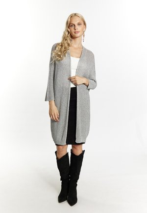 Grauer gestrickter Cardigan mit langen Ärmeln und offenem Vorderteil, kombiniert mit einem schwarzen Rock und kniehohen schwarzen Wildlederstiefeln. Glatte Textur.