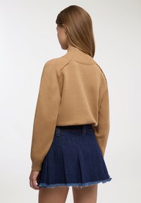 Maglione marrone lavorato a maglia con collo alto abbinato a una mini gonna in denim scuro con pieghe e bordo sfrangiato. Vista posteriore mostrata.