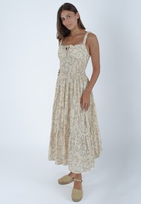 Jasno beżowa sukienka z kwiatowym wzorem, dopasowana w talii, z regulowanymi ramiączkami i warstwową spódnicą. W połączeniu z beżowymi espadrylami.