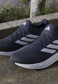 Running shoes with a dark navy mesh upper, white three-stripe design, cushioned sole, and textured gray outsole. Lightweight and flexible.