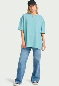 Üks suur ja hele sinine puuvillane T-särk lühikeste varrukatega, ümmarguse kaelusega ja tikandiga logoga, millele on kombineeritud lõdvad heledates tooni teksased ja spordijalatsid.