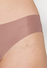 Light brown, seamless Sloggi underwear with a soft texture and elastic waistband. The brand logo is subtly printed on the side.