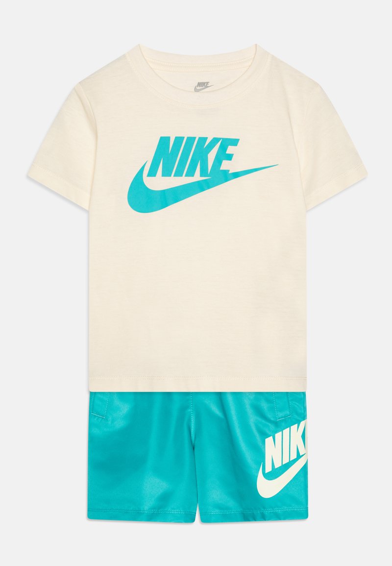 Bombažna kremna majica s turkiznim logotipom Nike, v kombinaciji s turkiznimi kratkimi hlačami, ki imajo beli logotip Nike, zasnovana za udobje in gibanje.