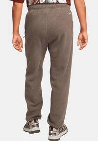 Bruna fleece-joggingbyxor med en mjuk textur, utrustade med sidofickor och ett elastiskt midjeband, tillsammans med grå och svarta löparskor.