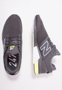 Šedé sportovní boty s prodyšným síťovaným svrškem, bílými akcenty, výrazným logem a polstrovaným límcem s kontrastním žlutým detailem.