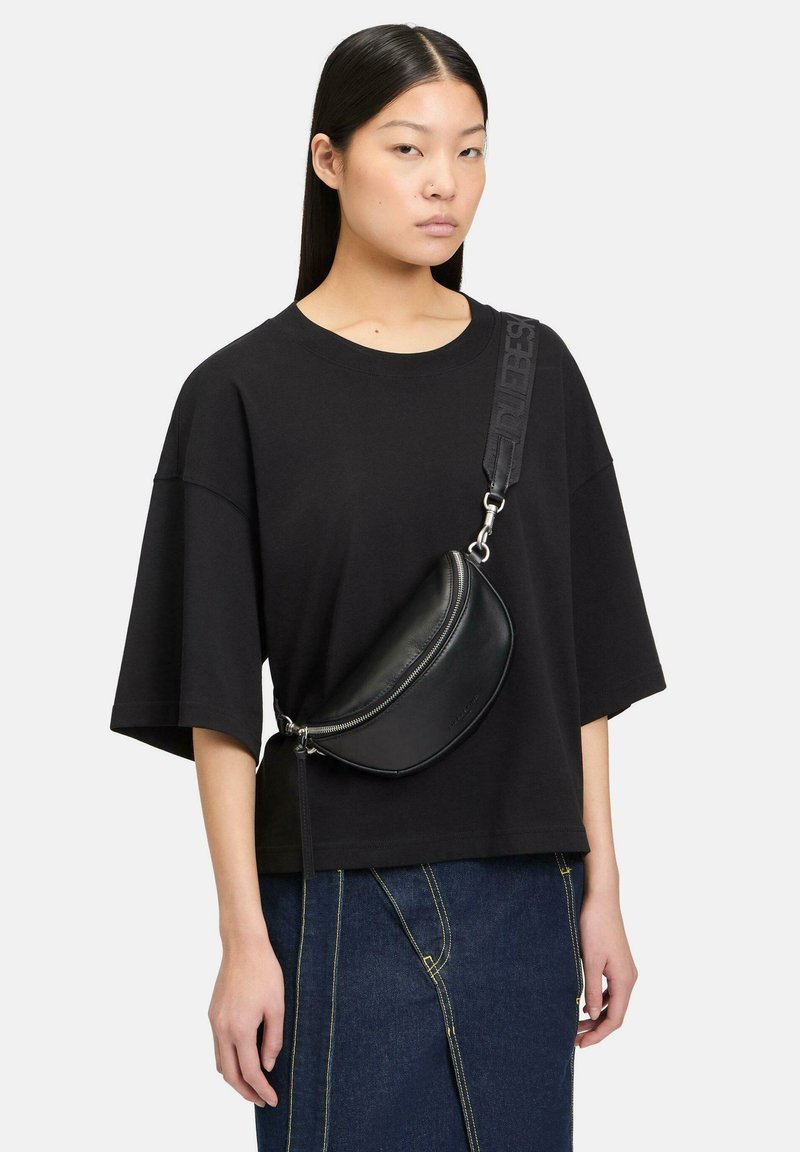 Borsa a tracolla in pelle nera con forma curva, accessori in argento e tracolla testurizzata. Indossata sopra una t-shirt nera morbida e una gonna di jeans.