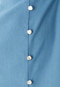 Zils audums ar reljefainu virsmu, vienā pusē vertikāli sakārtotas piecas pogas ar čaulu rakstu.