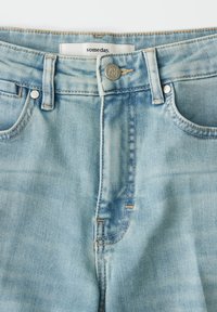 Lichtblauwe spijkerbroek met een vervaagde afwerking, voorzien van een gulp met knopen, vijf zakken en contrasterende stiksels. "someday." label zichtbaar aan de binnenkant van de tailleband.