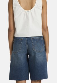 Τζιν σορτς με ψηλόμεση γραμμή, μπλε χρώμα, σχεδιασμό με πέντε τσέπες και ξέφτια στο τελείωμα. Συνδυασμένα με λευκό αμάνικο τοπ.