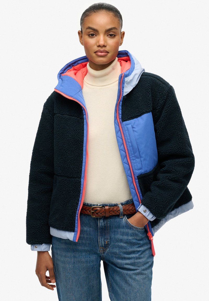 Zwarte fleecejas met blauwe en koraalkleurige accenten, ritssluiting, capuchon en gestructureerde stof; heeft contrasterende kleurvlakken en een voorzak.