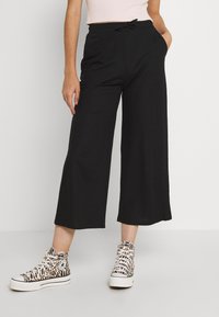 Pantalons larges noirs en tissu doux, dotés d'une taille élastique et d'un cordon de serrage. Associés à des baskets montantes à motifs.