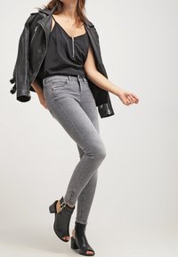 Jeans ajustados grises combinados con una blusa sin mangas negra y una chaqueta de cuero negra; botas de tobillo negras con puntas abiertas y herrajes dorados.