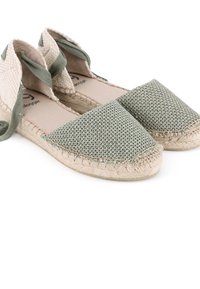Espadrilles trenzadas verdes con parte superior de lona texturizada, suela plana de yute y lazos de tela en los tobillos. Presentan un diseño de punta redonda.