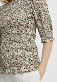 Blomstret bluse med samlet tekstur, prydet med pink og orange blomster på en grøn og sort baggrund. Puffærmer med flæsekanter.