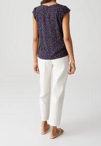 Haut bleu marine à petit motif à pois, manches courtes volantées et détail bouton en forme de goutte au dos, associé à un pantalon blanc droit.