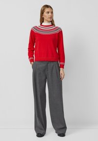Czerwony sweter z wzorzystą narzutką, ozdobiony białymi wzorami. W zestawieniu z luźnymi szarymi spodniami o swobodnym kroju i plisowanym detalu.
