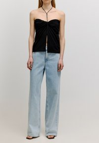 Schwarzes trägerloses Oberteil mit gerafftem Stoff an der Brust, kombiniert mit locker sitzenden hellblauen Jeans. Der Look wird mit schwarzen Sandalen abgerundet.