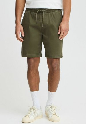 Olijfgroene shorts gemaakt van zacht stof, met een elastische tailleband met trekkoord en zijzakken. Gestyled met witte sneakers en sokken.
