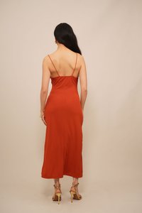 Roodbruine ribbel midi-jurk met dunne bandjes, aansluitende lijfje en split aan de onderkant. Draagt met tan hoge hakken sandaaltjes. Gladde textuur.