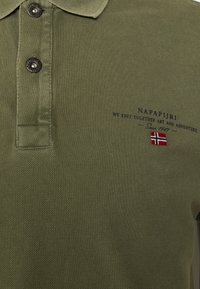 Olivgrön pikétröja med två svarta knappar och broderad norsk flagga samt Napapijri-logotyp med slogan på bröstet.