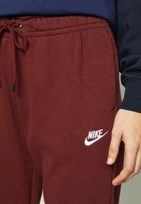 Maroon bomullssweatpants med elastisk midja och justerbar dragkedja. Har en vit Nike-logga på vänster lår.