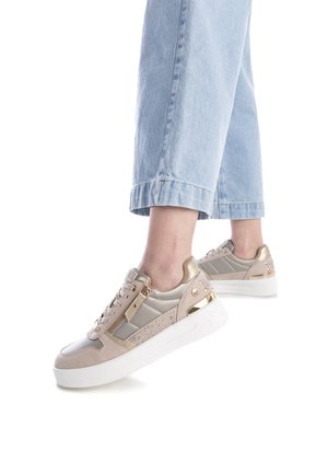 Zapatillas beige y oro con una mezcla de materiales lisos y texturizados, presentando acentos decorativos, una suela blanca gruesa y un zipper lateral.