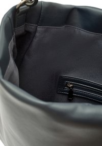 Inredningen av läderhandväskan är i mörk marinblå med en slät yta. Den har en blixtlåsficka med en svart dragflik och en tygfoder.