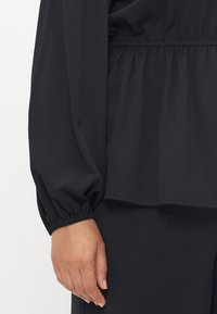 Black, long-sleeve top with a gathered waistline and elastic cuffs. Lightweight fabric with a smooth texture, featuring a relaxed fit.
