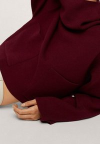 Burgunderfarbenes, übergroßes Sweatshirt mit einem Schalkragen, featuring Vordertaschen und langen, locker sitzenden Ärmeln. Weicher, strukturiert gestrickter Stoff.